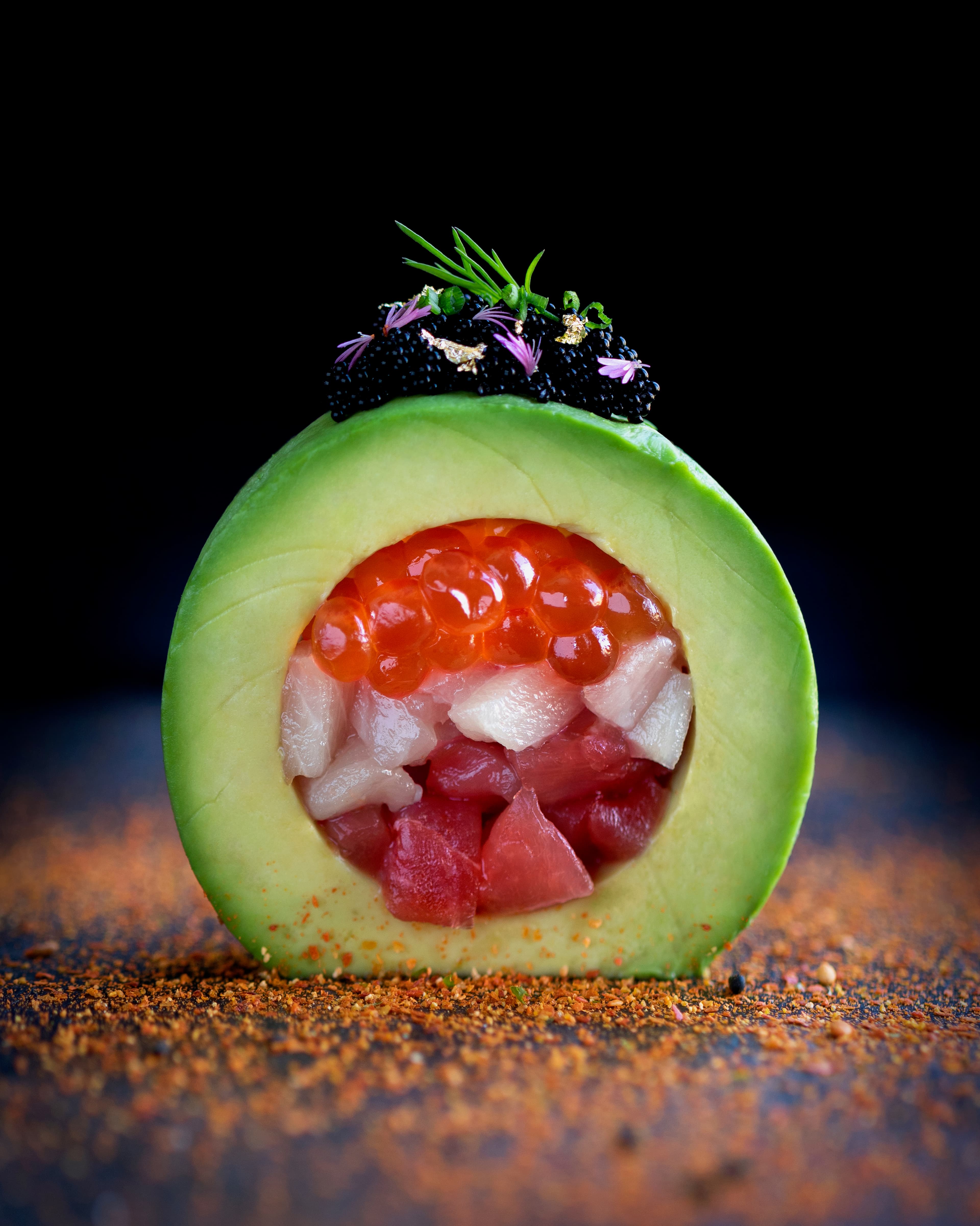 Avocado sliced into a ring and filled with diced tuna and yellowtail, topped with caviar, gold leaf, and edible flowers