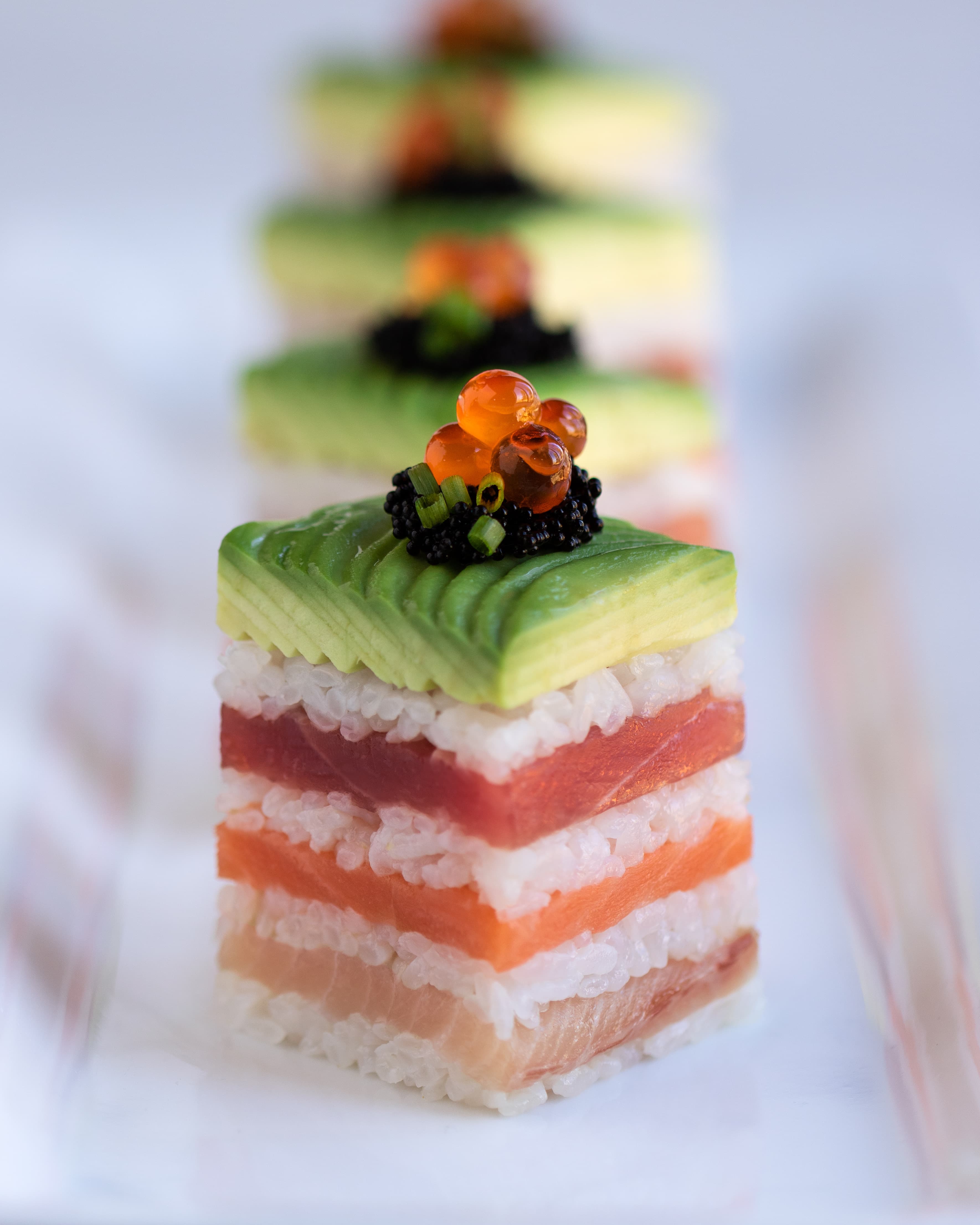 Square pressed sushi blocks layered with tuna, salmon, rice, and avocado, topped with roe and caviar