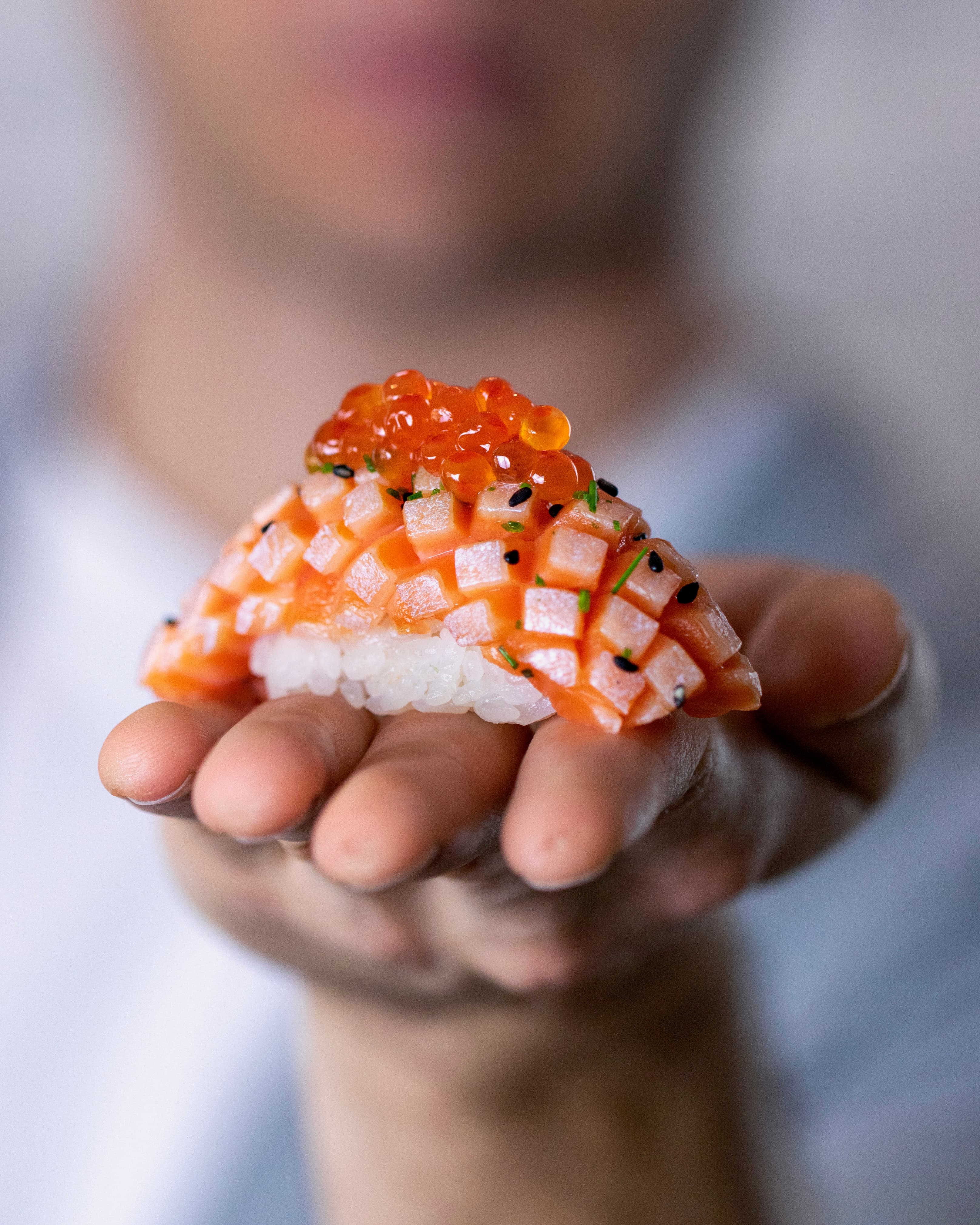 Hand holding a diced salmon and tuna sushi piece topped with salmon roe and sesame seeds