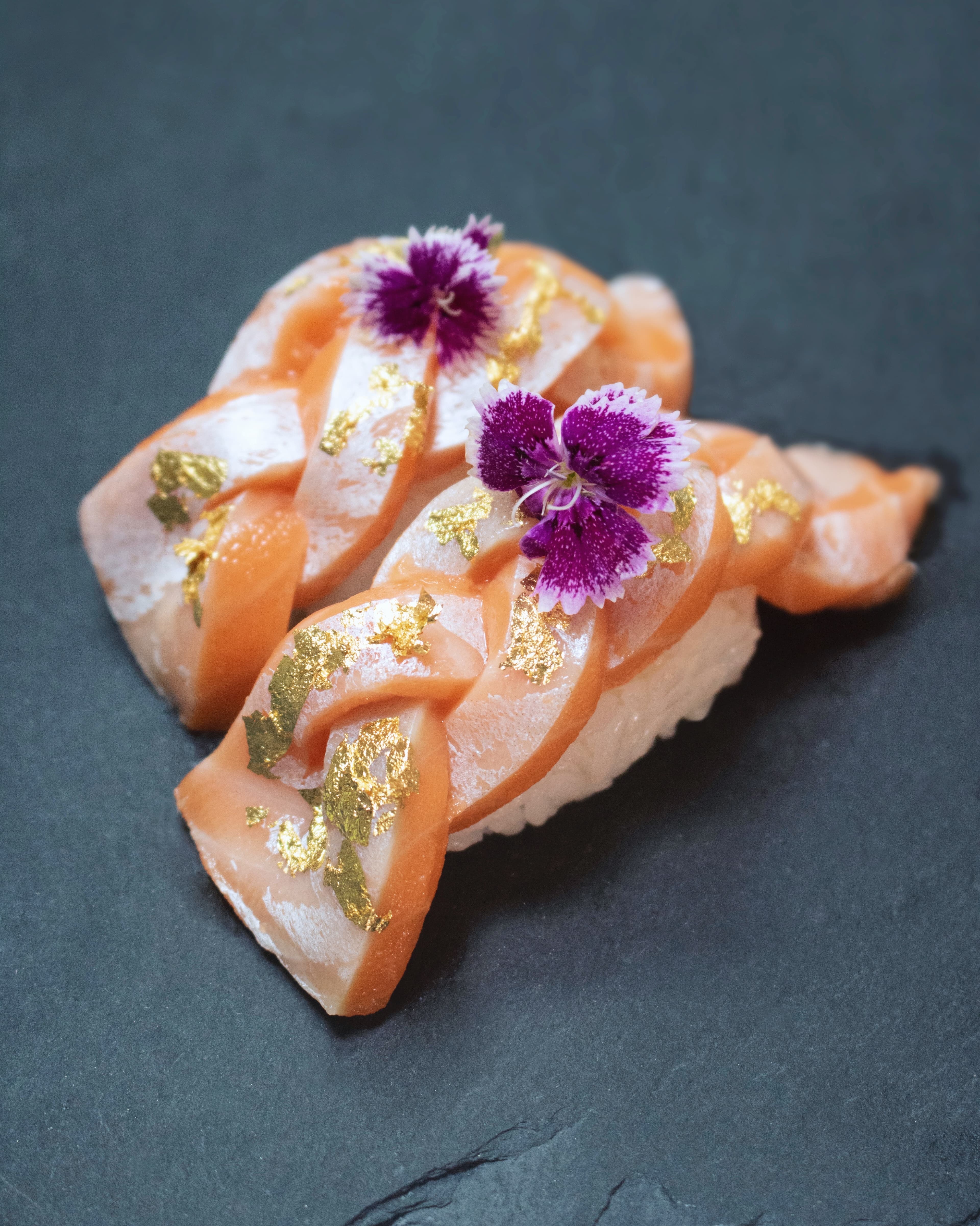 Nigiri topped with braided salmon, gold leaf, and purple edible flowers
